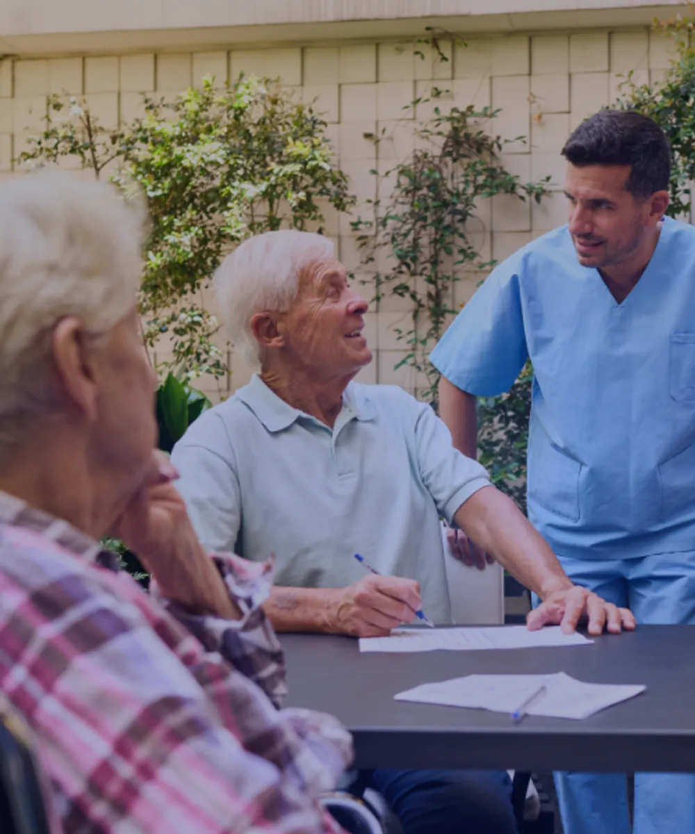 Aged care professional in blue scrubs reviewing medical records with an elderly resident, representing clinical risk and professional indemnity insurance for aged care providers.