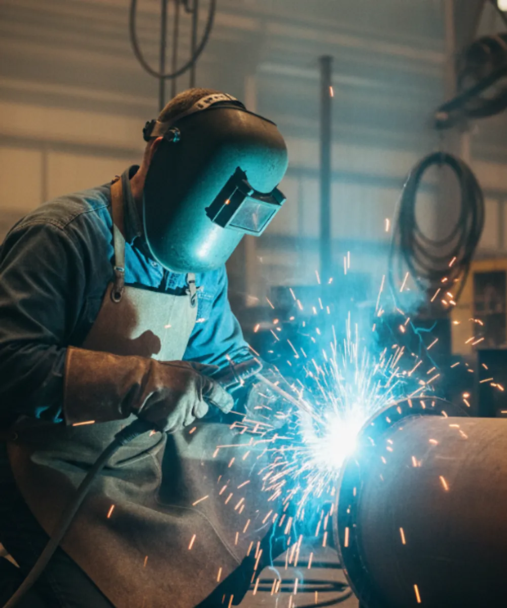 Professional boilermaker in full protective gear performing structural steel welding, representing hot works and liability insurance for welders.
