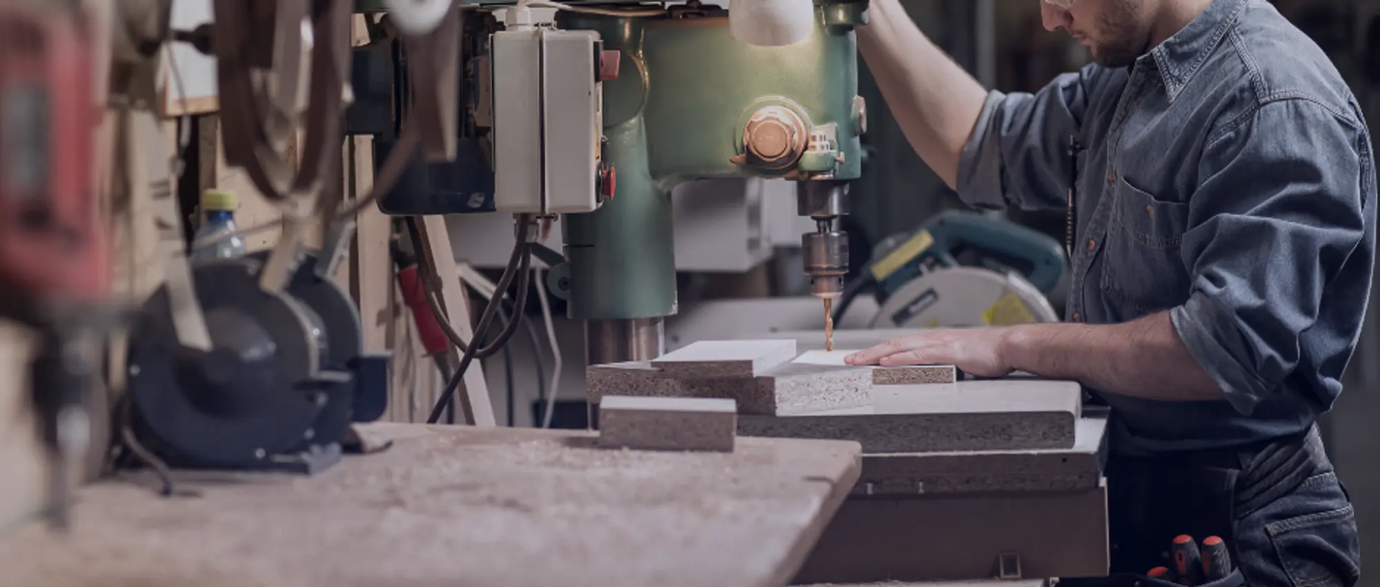 Close-up of specialist carpentry tools including a power drill and chisels on a workshop bench with wood shavings.