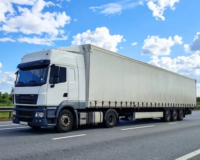 Large white semi-trailer truck performing freight transport on a highway, depicting standard heavy vehicle insurance for logistics businesses.