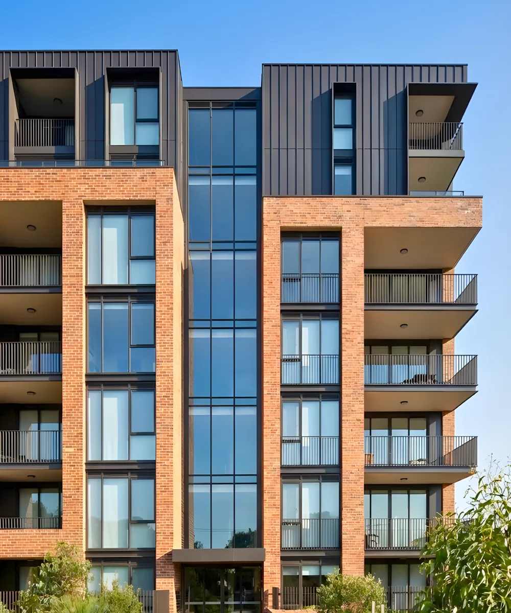 Detailed front facade of a multi-story strata-titled apartment building showing a mix of brickwork, glass windows, and modern metal cladding.