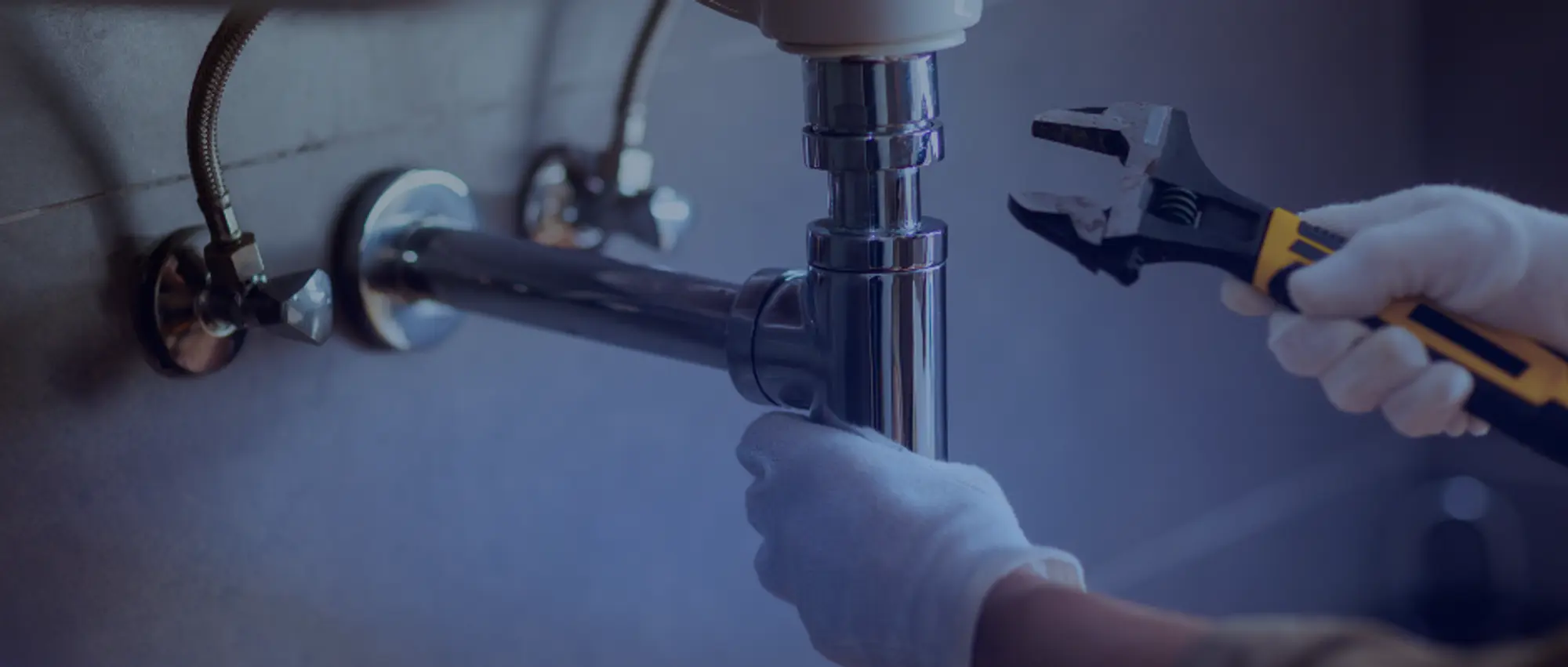 Handyman using adjustable wrench to repair chrome sink plumbing pipes during a residential maintenance job