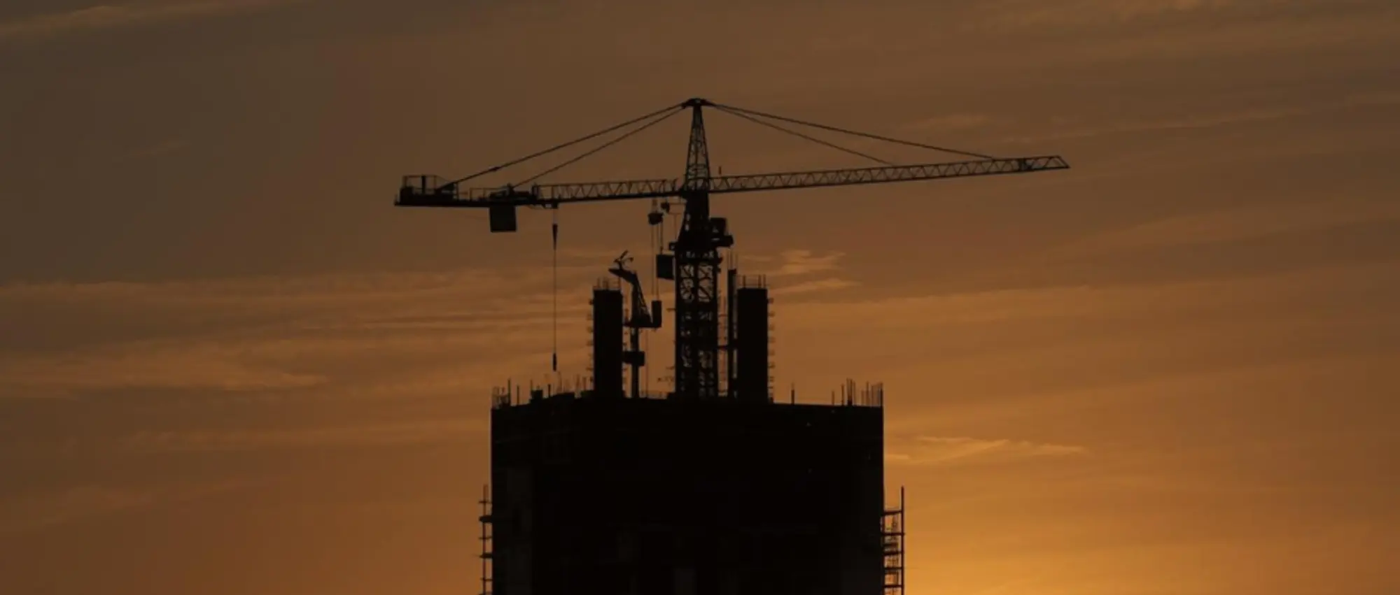 Tower crane silhouette on high-rise construction site at sunset