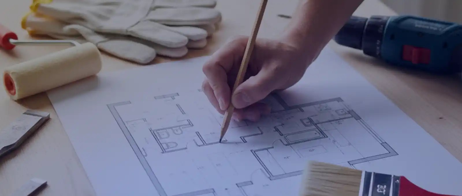 Home renovator drafting architectural floor plan with paint roller, work gloves, and power drill for residential renovation project