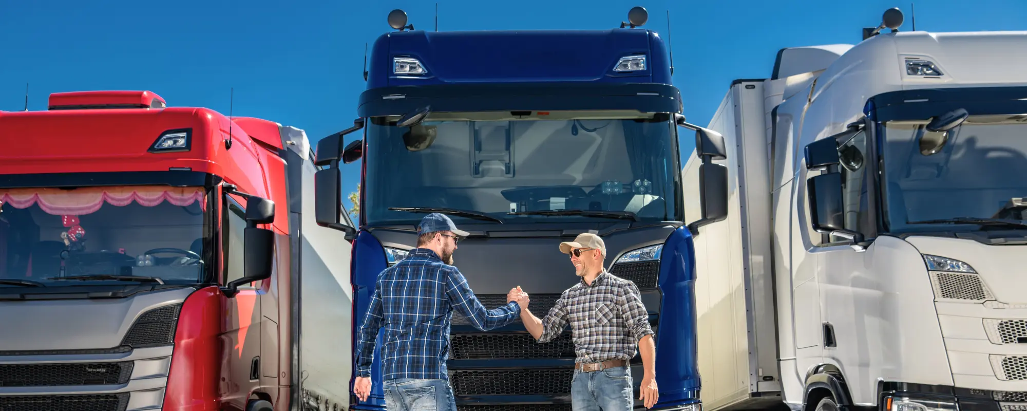 Two truck drivers shaking hands in front of their prime movers, signifying trust, partnership, and successful truck insurance claims or handovers.