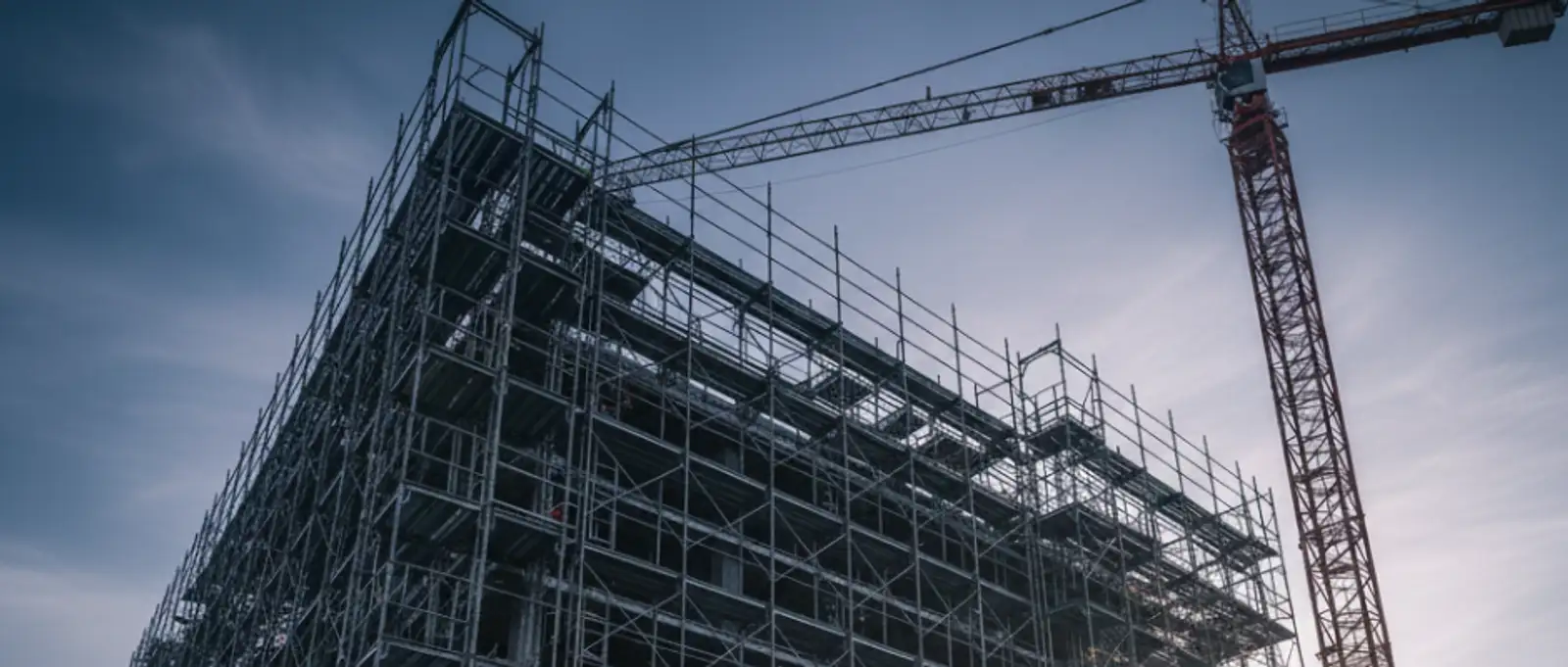 Industrial scaffolding framework on a commercial building with tower crane against overcast sky